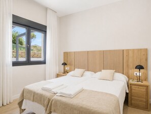 Een slaapkamer met een groot bed, twee nachtkastjes, een houten hoofdeinde en een raam met gordijnen.