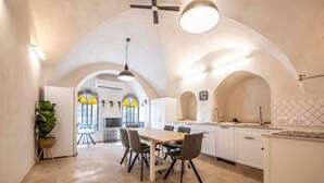 Una cocina amplia con comedor, armarios blancos y un techo alto con arquerías.