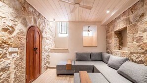 Una habitación acogedora con pared de piedra, puerta de madera, sofá seccional gris y ventilador de techo.
