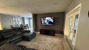 Ein modernes Wohnzimmer mit einem Ecksofa, einem an der Wand befestigten Flachbildfernseher und einem Essbereich im Hintergrund.
