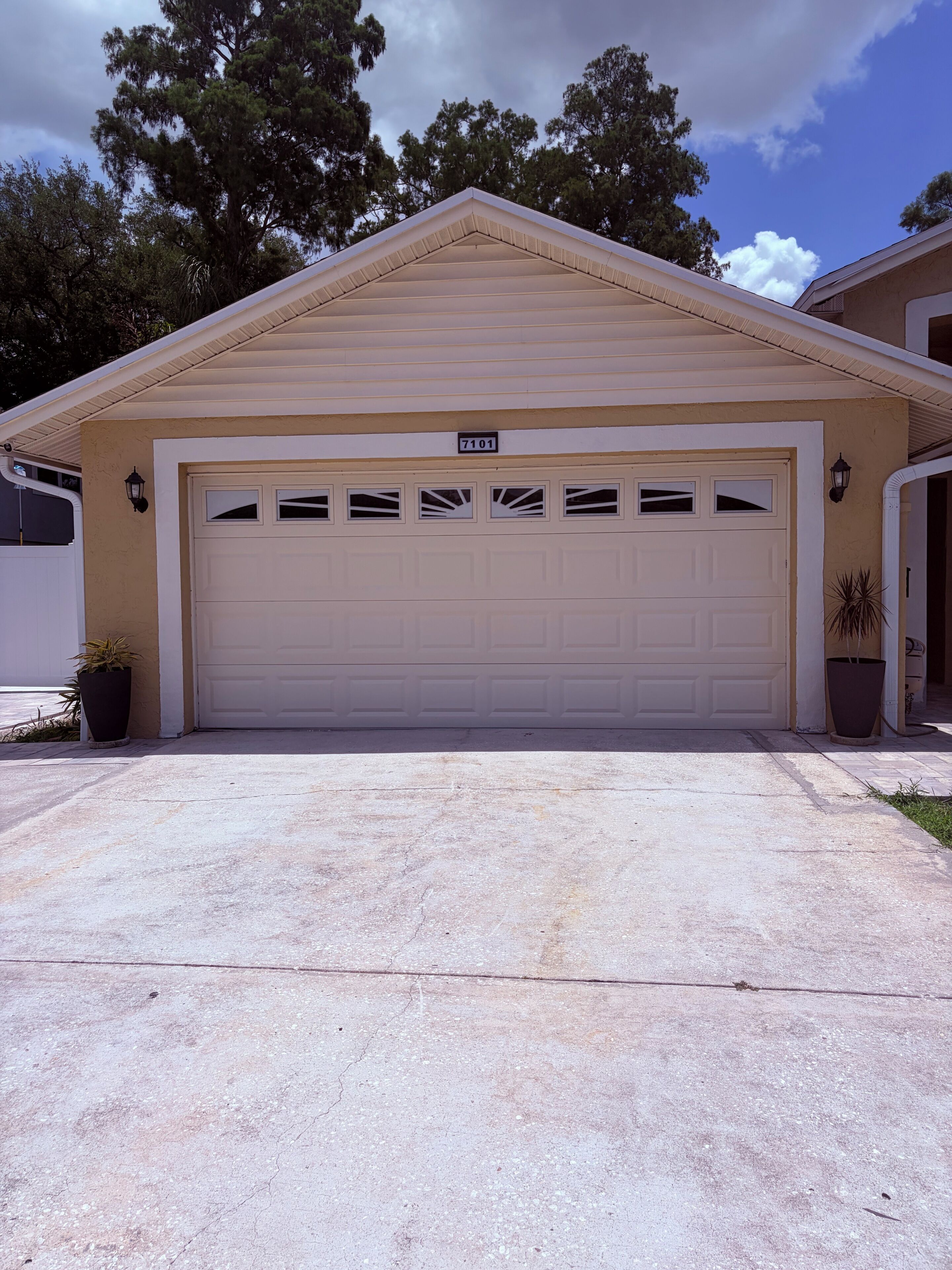 A single-story house with a garage, a number plate, and a potted plant.
