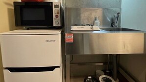 A compact kitchenette with a microwave, a small refrigerator, a sink, and a trash bin.