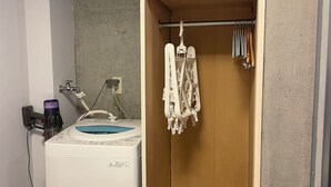 A compact laundry area with a washing machine, a drying rack, and a small shelf.