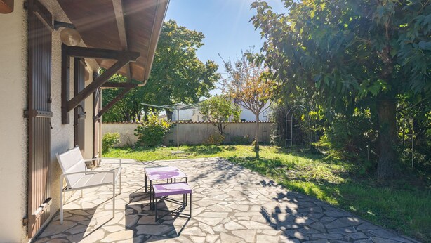 Un patio con piso de piedra, dos sillas blancas y una mesa morada.