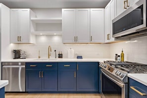 A modern kitchen with white cabinets, a blue countertop, stainless steel appliances, and gold handles.