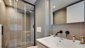 A modern bathroom with a glass shower enclosure, a white sink, and toiletries on the countertop. - Pleasant and Bright apt - 1bd/2p - Near Paris (Aubervilliers)