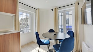 A modern room with a round table, blue chairs, a wooden cabinet, and large windows with curtains. - Pleasant and Bright apt - 1bd/2p - Near Paris (Aubervilliers)