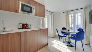 A modern kitchen with wooden cabinets, a built-in microwave, and a dining area with blue chairs and a table. - Pleasant and Bright apt - 1bd/2p - Near Paris (Aubervilliers)