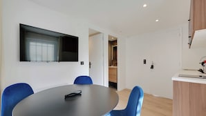 A modern room with a round table, blue chairs, a flat-screen TV mounted on the wall, and a small kitchenette area. - Pleasant and Bright apt - 1bd/2p - Near Paris (Aubervilliers)
