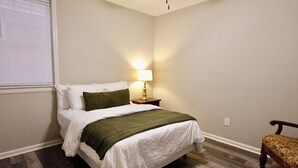 A bedroom with a bed, a nightstand with a lamp, a chair, and a ceiling fan. - 3BR Basement Apartment Close to CU (Central)