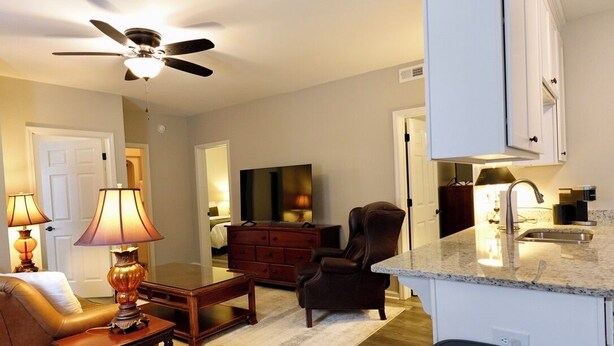 A living room with a sofa, a coffee table, a TV, and a fireplace. There is a kitchen area with a sink and cabinets. - 3BR Basement Apartment Close to CU (Central)