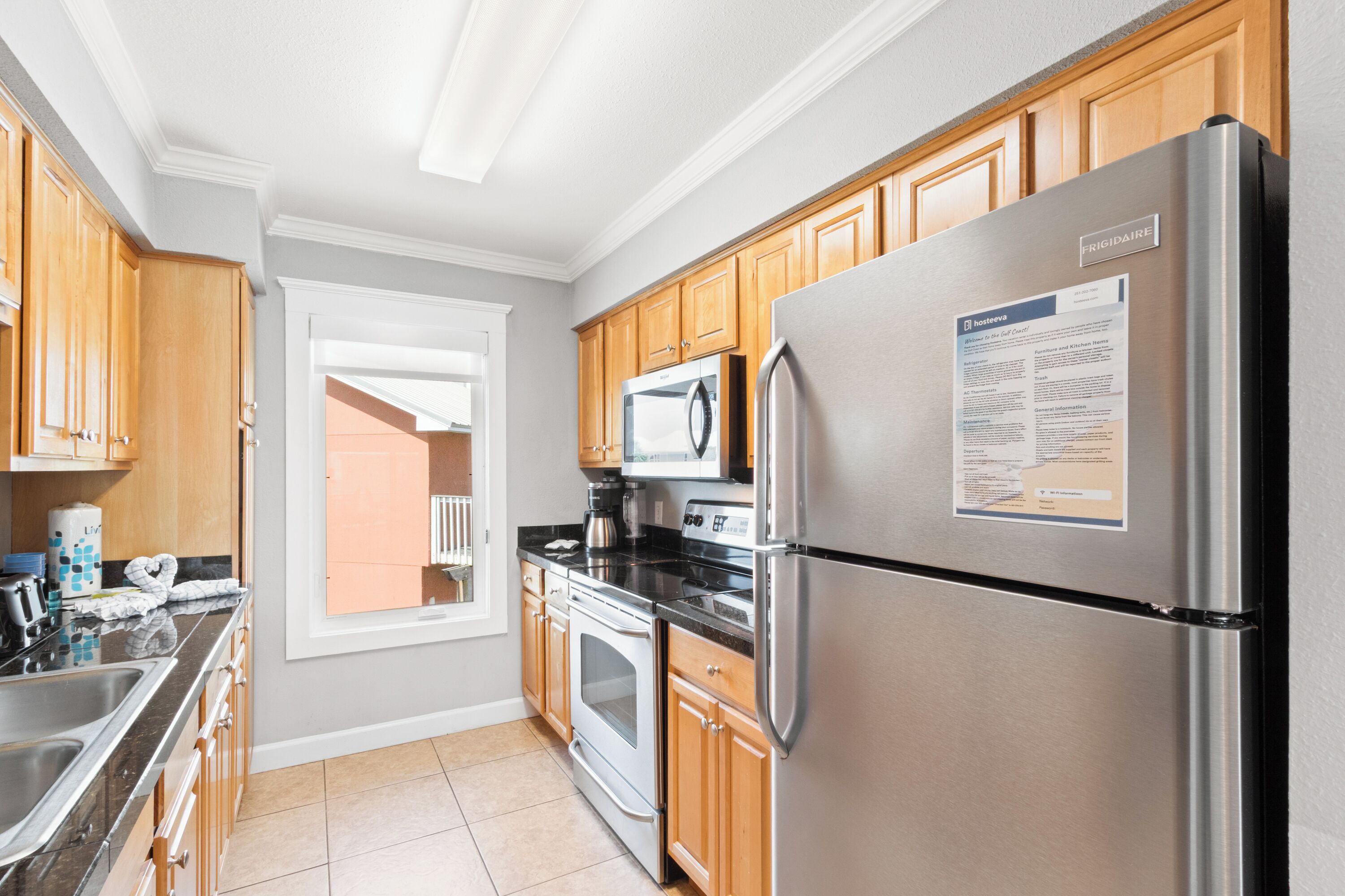 A modern kitchen with stainless steel appliances, wooden cabinets, and a large window.