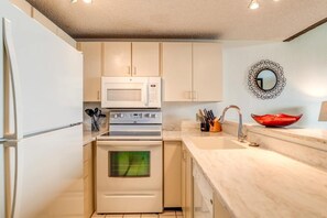 Cocina compacta con armarios blancos, microondas, horno, pileta y un espejo decorativo.
