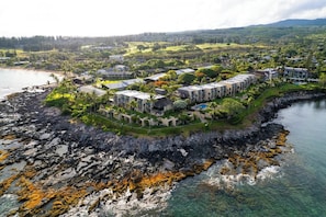 A coastal hotel with multiple buildings, a rocky shoreline, and clear water.