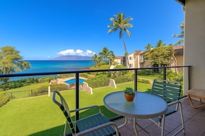 A balcony with a view of the ocean, a pool, and a small garden.