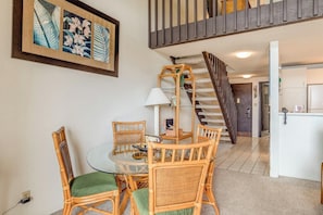 Un espace repas aménagé avec des meubles en osier, une table en verre et un escalier menant à un niveau supérieur.