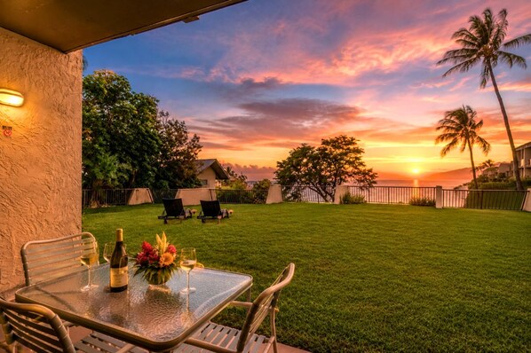 Eine Terrasse mit Tisch für zwei Personen, mit Blick auf eine Rasenfläche und einen Sonnenuntergang.