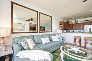 Ein Wohnzimmer mit einem grauen Sofa, zwei großen Spiegeln, einem Deckenventilator und einer Küche im Hintergrund.