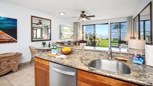 Una cocina moderna con encimera de granito, pileta de acero inoxidable y vistas al océano a través de amplios ventanales.
