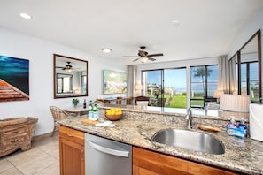 A modern kitchen with a granite countertop, stainless steel sink, and a view of the ocean.
