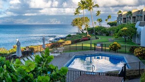 A pool area with a view of the ocean, surrounded by palm trees and a well-maintained lawn. - Napili Point | Oceanfront 3 BR, Sleeps 8 | Car Incl. w/ 6+ Nights | NAP ML-1556 by KBM (Lahaina)
