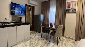 A modern hotel room with a kitchen area, a dining table with chairs, a flat-screen TV mounted on the wall, and a painting of the Eiffel Tower. - Zayed Plaza (Sheikh Zayed City)