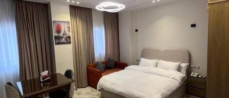 Una habitación de hotel moderna con una cama grande, una mesa de comedor con sillas, un armario de madera y una alfombra con diseño de mármol.