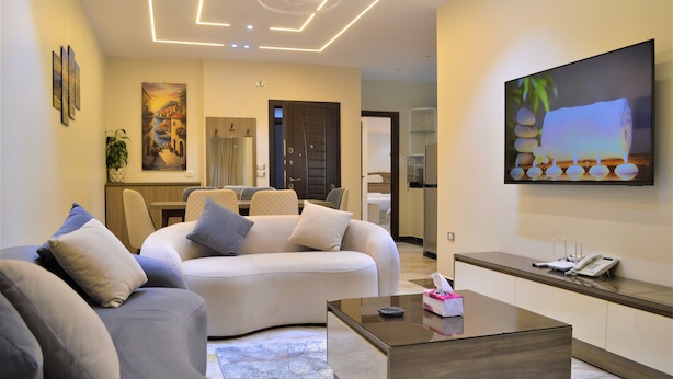 A modern living room with a sofa, a coffee table, and a flat-screen TV mounted on the wall. - Zayed Plaza (Sheikh Zayed City)