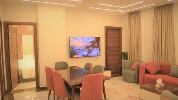 A modern living room with a dining area, a TV mounted on the wall, and a large window with curtains.