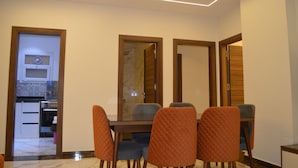 A dining area with a glass-top table and four chairs, a kitchen visible through an open door, and a modern ceiling design. - Zayed Plaza (Sheikh Zayed City)