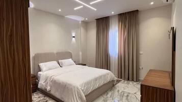 A modern bedroom with a large bed, a wooden wardrobe, a marble-patterned rug, and recessed ceiling lighting.
