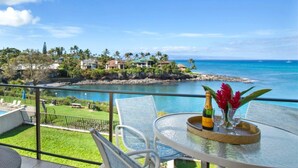 A balcony with a glass table, chairs, a bottle of champagne, and a vase with flowers. - Napili Point | Oceanfront 5 BR, Sleeps 14 | Car Incl. w/ 6+ Nights | NAP ML-1571 by KBM (Lahaina)