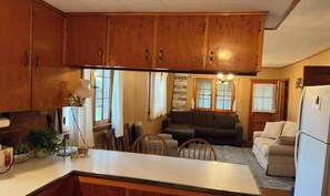 A kitchen with wooden cabinets, a central island, and a dining area with a couch and chairs. - Rustic 3-bedroom cottage in Windsor. (Windsor)