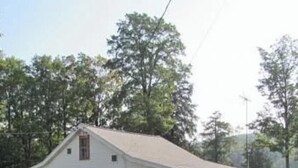 A single-story white building with a gabled roof, a front porch, and a fenced yard.