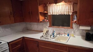 A compact kitchen with wooden cabinets, a white countertop, a sink, and a stove.