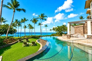 A pool area with a curved design, lounge chairs, and a view of the ocean.