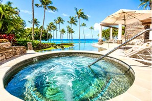 A hot tub with a view of the ocean, surrounded by palm trees and lounge chairs.