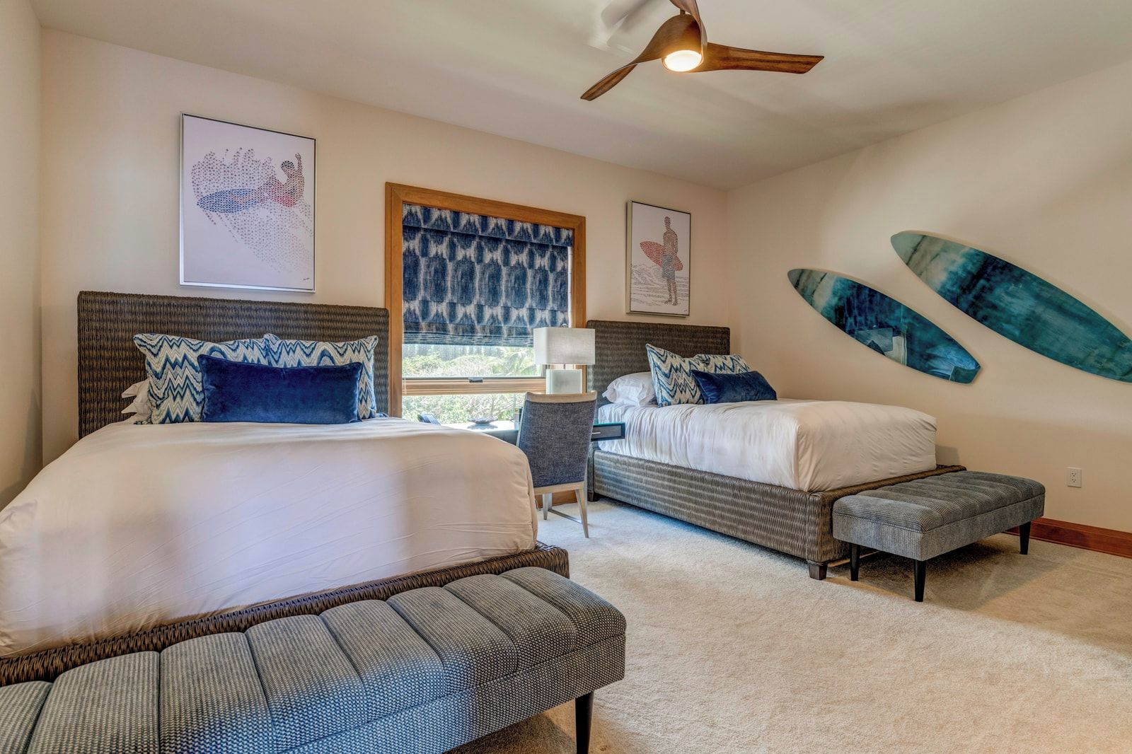A bedroom with two beds, a window, a desk, and artwork on the walls.