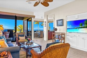 A spacious living area with a large TV, comfortable seating, a dining area, and a view of the ocean.