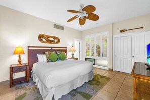 A hotel room with a bed, two bedside tables with lamps, a ceiling fan, a door with a view, and a television.