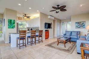 A spacious living area with a blue sofa, a coffee table, and a kitchen with a bar area. - Kapalua Bay | Ocean View 4 BR, Sleeps 12 | Car Incl. w/ 6+ Nights | KBV ML-1601 by KBM (Lahaina)