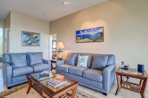 A living room with two grey sofas, a glass coffee table, a lamp, and a painting of a beach scene.