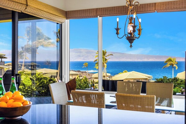 A dining area with a view of the ocean, wicker furniture, and a chandelier.
