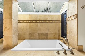 A large, rectangular bathtub with a glass ceiling above, beige tiled walls, and a small window on the right.