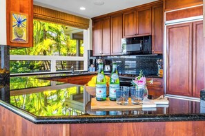 A kitchen with wooden cabinets, a stainless steel microwave, and a large window with a view of greenery.