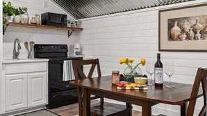 Una cocina con armarios blancos, una estufa negra y una mesa de madera adornada con flores, una botella de vino y copas.