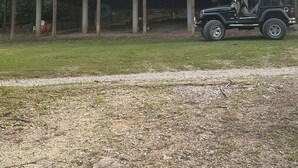 Una cabaña de madera de dos pisos con un balcón, un Jeep estacionado en frente y un área verde al frente.