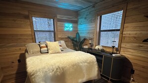 Un dormitorio con paneles de madera, una cama, un escritorio y un letrero de neón.