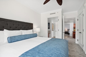 Hotellihuone, jossa on suuri sänky, kattotuuletin ja näkymä käytävälle.