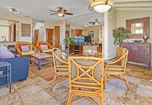 A spacious living area with wicker furniture, a glass-top dining table, ceiling fans, and a television.